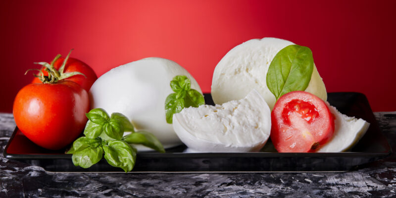 Mozzarella cheese with fresh tomatoes and basil on black and red background.