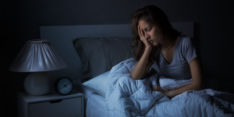 Depressed young Asian woman sitting in bed cannot sleep from insomnia